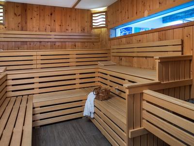 Dřevěná sauna s víceúrovňovými lavicemi, košíkem a ručníkem, teplé vnitřní osvětlení.