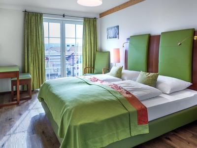 Moderní hotelový pokoj se zelenou postelí, dřevěnou podlahou a balkonem se záclonami.