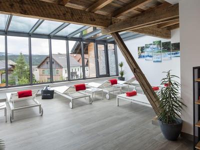 Světla hotelová hala s velkými okny, bílými židlemi a červenými polštáři s výhledem na hory.