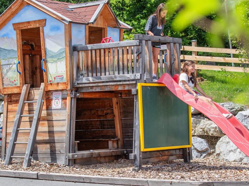 Hrací domek s klouzačkou a malovanou fasádou v hotelovém venkovním prostoru