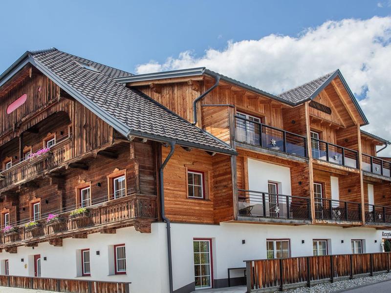 Pohodlný hotel s dřevěnou fasádou a balkony pod modrou oblohou.