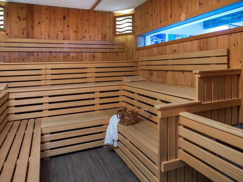 Dřevěná sauna s víceúrovňovými lavicemi, košíkem a ručníkem, teplé vnitřní osvětlení.