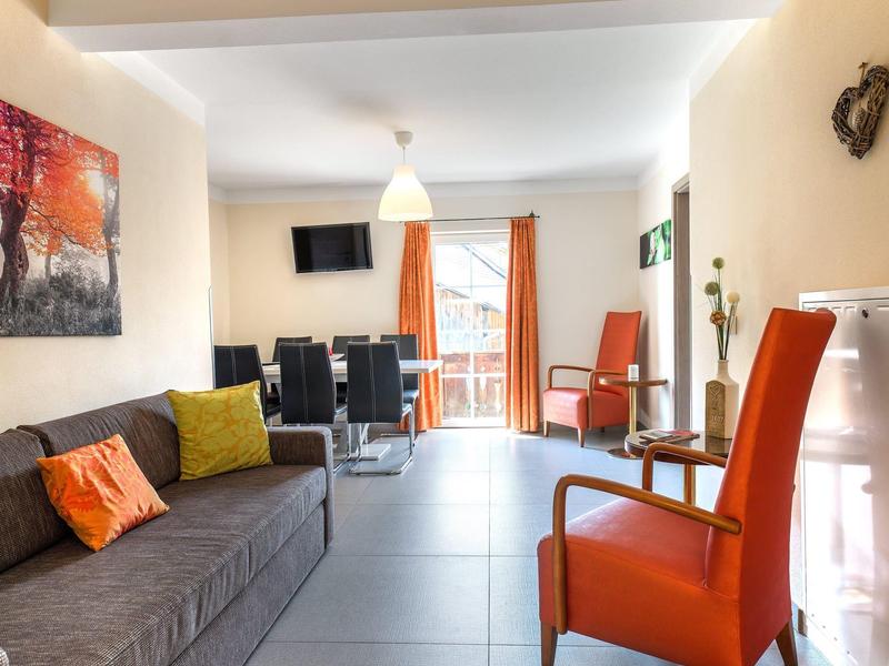 Moderně zařízený obývací pokoj se šedou pohovkou a oranžovými křesly v světlé místnosti.