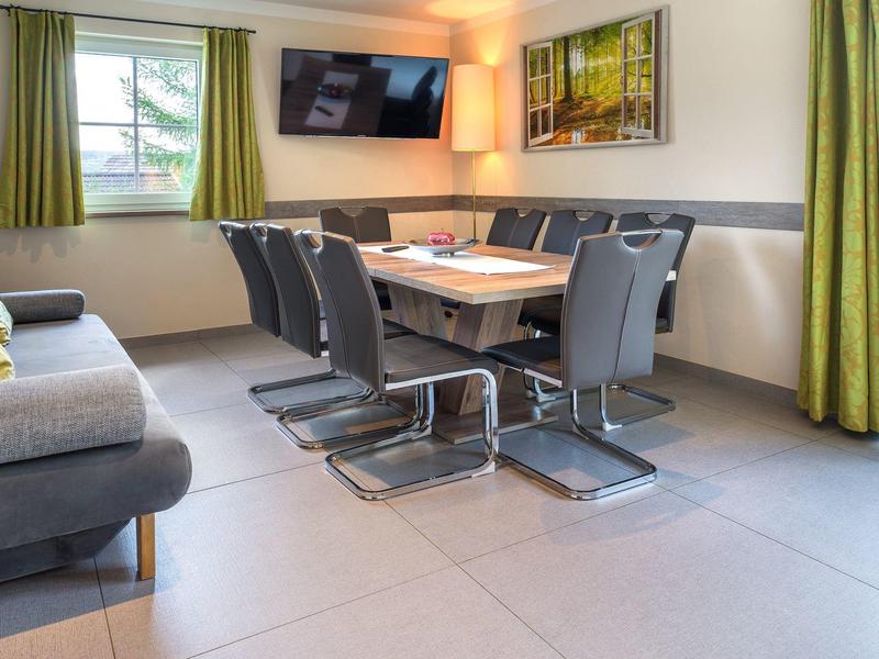 Moderní zasedací místnost s tmavými židlemi, velkým stolem, televizí a zeleno-žlutými závěsy.