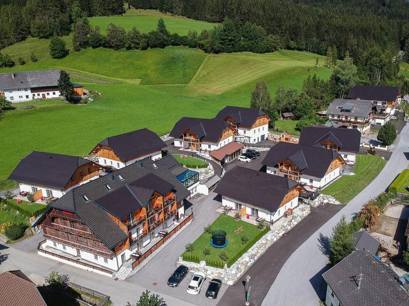 Letecký pohled na resort s několika chatkami obklopený zelenými loukami a lesem.