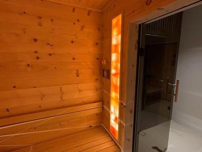 Sauna en bois avec banc et panneau éclairé à côté d'une porte en verre.