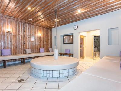 Salle de détente lumineuse avec banquette ronde rembourrée, murs en bois et carrelage blanc.