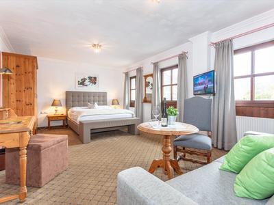 Chambre d'hôtel spacieuse avec un grand lit, un canapé gris et des fenêtres lumineuses.