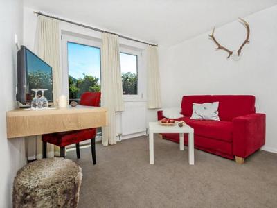 Salon confortable avec canapé rouge, télévision et fenêtre offrant une vue sur la verdure.