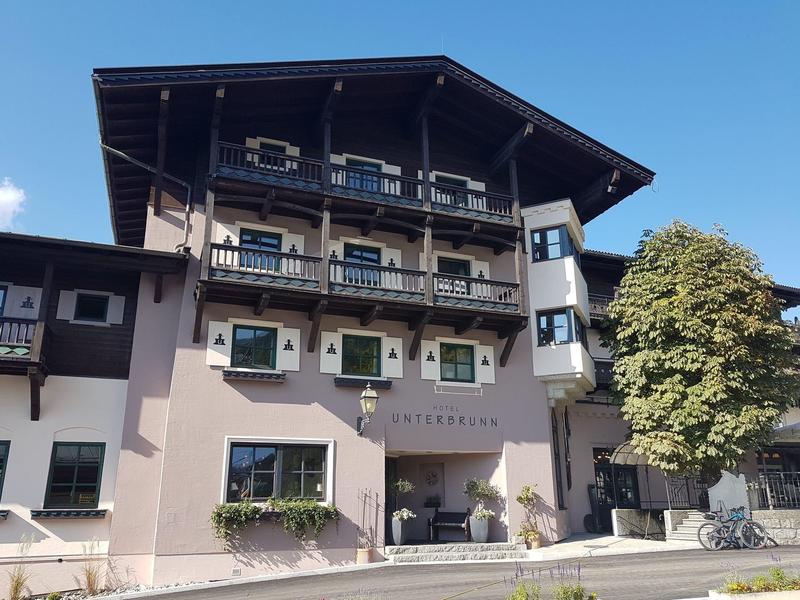 Hôtel traditionnel à plusieurs étages avec balcons en bois et volets verts à côté d'un arbre.