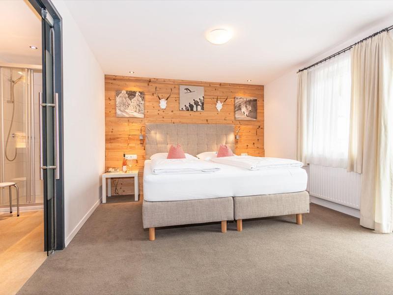 Chambre d'hôtel lumineuse avec lit double, mur en bois et salle de bain attenante avec douche.