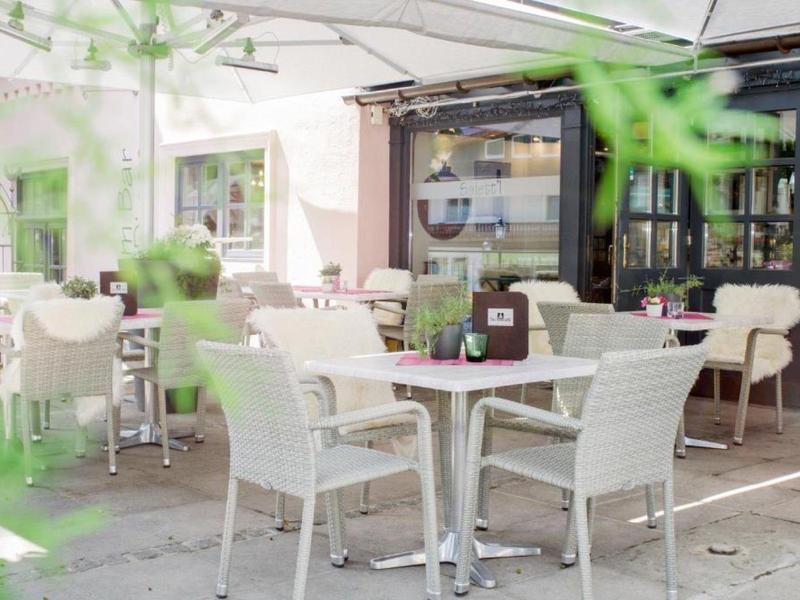 Terrasse lumineuse d'un café avec tables et chaises blanches sous de grands parasols.