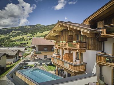 Hotel s dřevěnými balkony před zelenými kopci a modrou oblohou