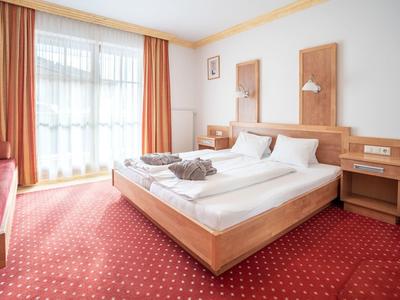 Světý hotelový pokoj s manželskou postelí, červenými závěsy a kobercem.