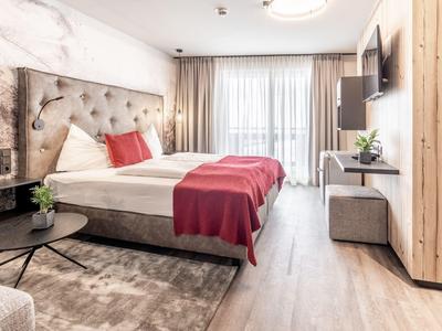 Světý hotelový pokoj s manželskou postelí, červenými akcenty a moderním zařízením.