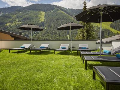 Lehátka s deštníky na zeleném trávníku s horami v pozadí.