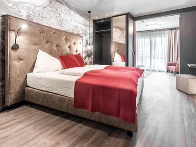 Moderní hotelový pokoj s velkou postelí a červenými doplňky.