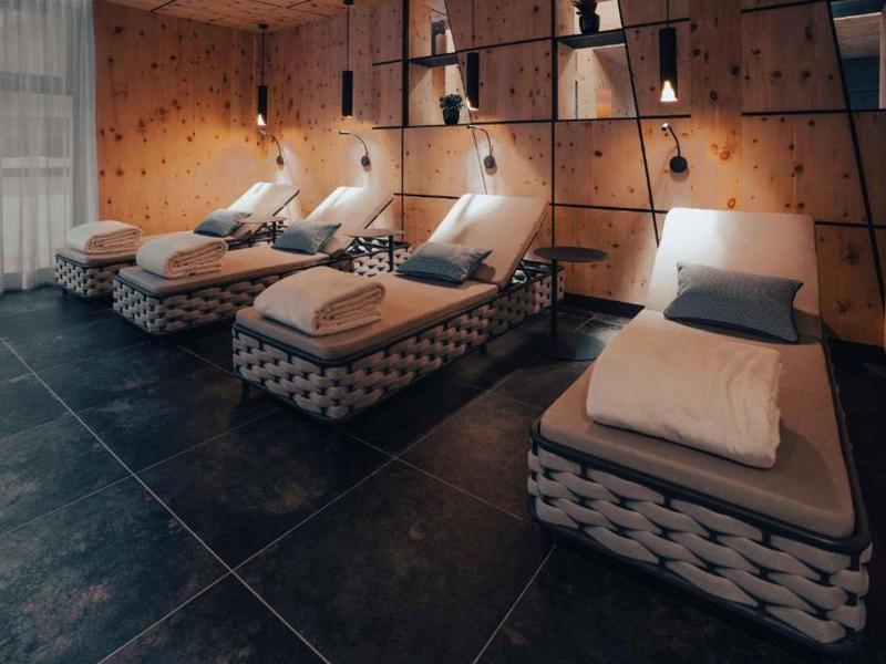 Tmavá wellness místnost se čtyřmi lehátky, měkkými polštáři a dekami.