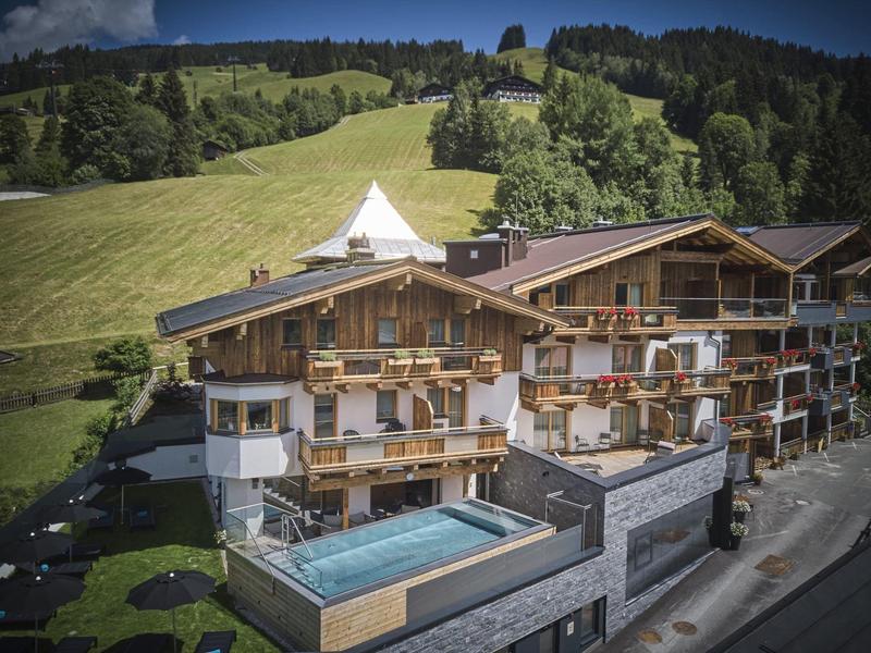 Alpský hotel s bazény a zelenými kopci v pozadí.