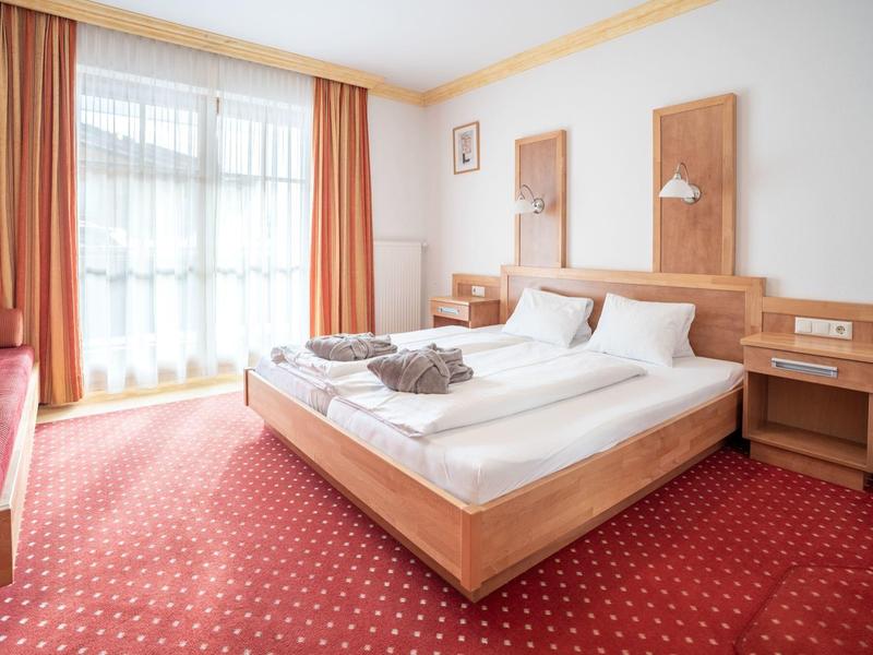 Světý hotelový pokoj s manželskou postelí, červenými závěsy a kobercem.