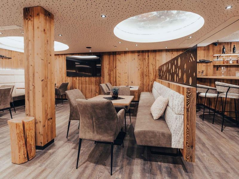 Pohodlná hotelová lounge s dřevěnými stěnami, čalouněnými židlemi a kulatými stropními světly.