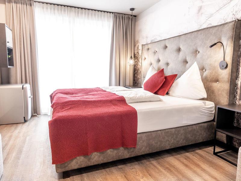 Světlá ložnice s velkou postelí a červenými doplňky.