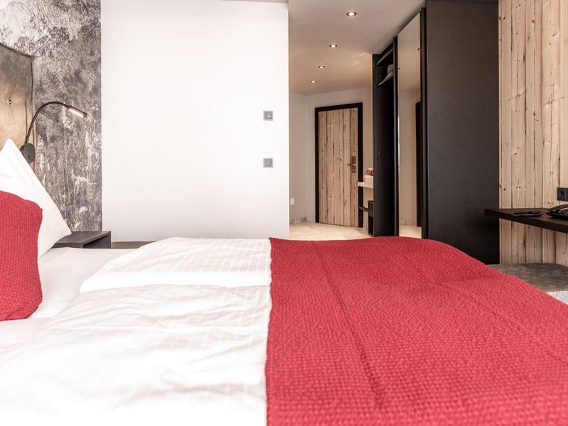 Moderní hotelový pokoj s pohodlnou postelí, červeným přehozem a dřevěnými doplňky.