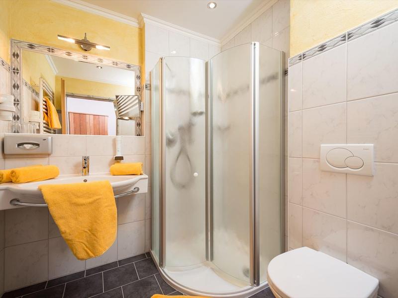 Malá koupelna se sprchou, umyvadlem a žlutými ručníky.