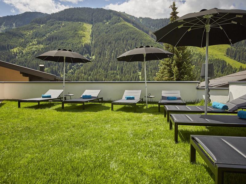 Lehátka s deštníky na zeleném trávníku s horami v pozadí.