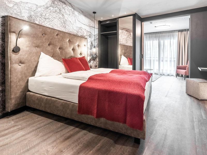 Moderní hotelový pokoj s velkou postelí a červenými doplňky.