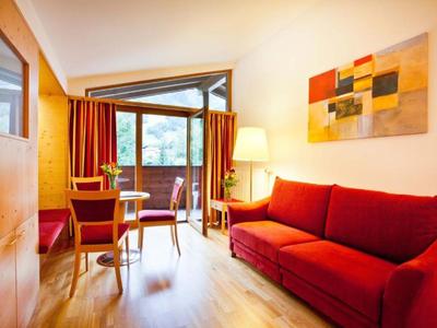 Gemütlicher Hotelraum mit rotem Sofa, Holzmöbeln und Balkon mit Blick ins Grüne.