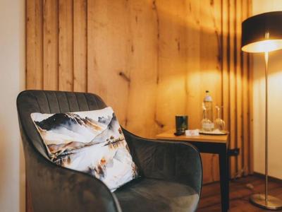 Bequemer Sessel mit Bergmotiv-Kissen neben einem runden Tisch und Stehlampe in warm beleuchtetem Raum.