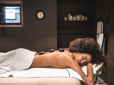 Frau entspannt sich bei Hot-Stone-Massage in ruhigem Spa-Zimmer.