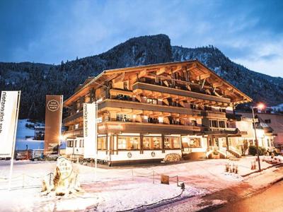 Beleuchtetes Hotel im Chalet-Stil mit verschneitem Berg im Hintergrund bei Abenddämmerung.