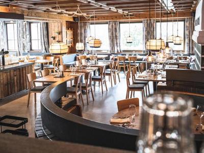 Gemütliches, gut beleuchtetes Restaurant mit Holzmöbeln und großer Fensterfront.