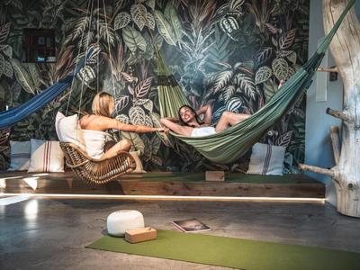 Zwei Personen entspannen in Hängematten in einem tropisch dekorierten Innenraum.