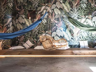 Gemütliche Hängematten und Kissen vor einer blätterreichen Wanddekoration in einem entspannten Raum.