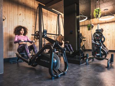 Frau trainiert auf einem Rudergerät in einem modernen Fitnessraum mit Holzverkleidung.