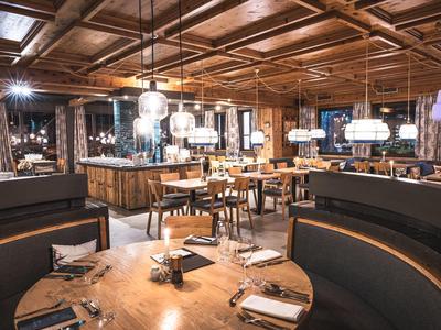 Gemütliches Restaurant mit Holztischen, halbrunden Sitzbänken und warmem Deckenlicht.