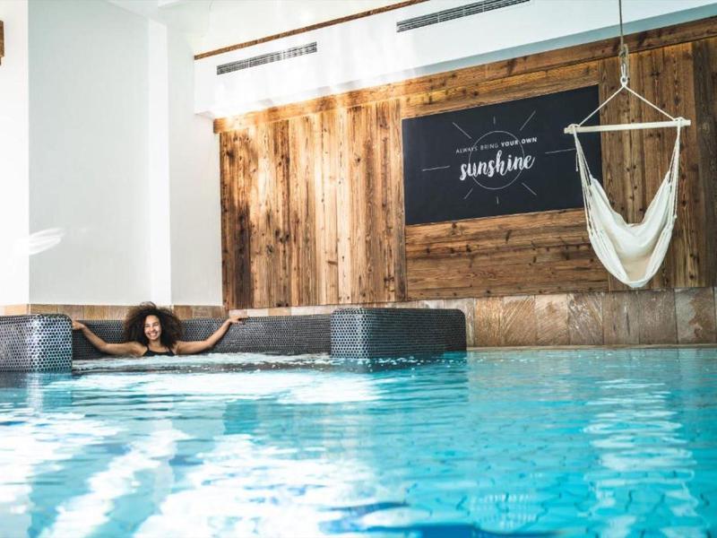 Innenpool mit einer Frau, die entspannt an der Kante lehnt, und einem Hängesessel an der Wand