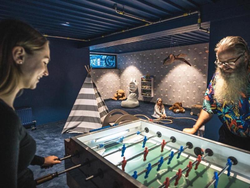 Zwei Personen spielen Tischfußball in einem stilvollen, dunklen Raum mit Zelt und gemütlicher Atmosphäre.