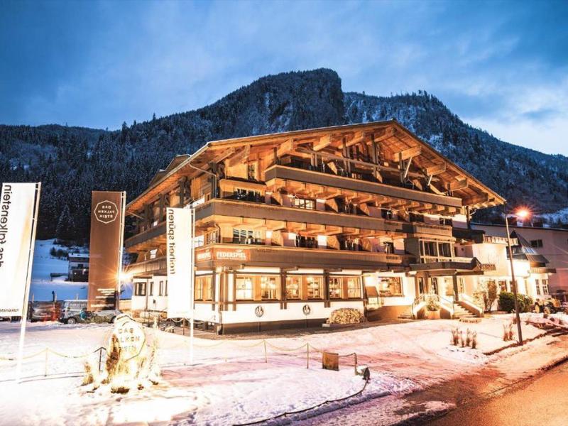 Beleuchtetes Hotel im Chalet-Stil mit verschneitem Berg im Hintergrund bei Abenddämmerung.
