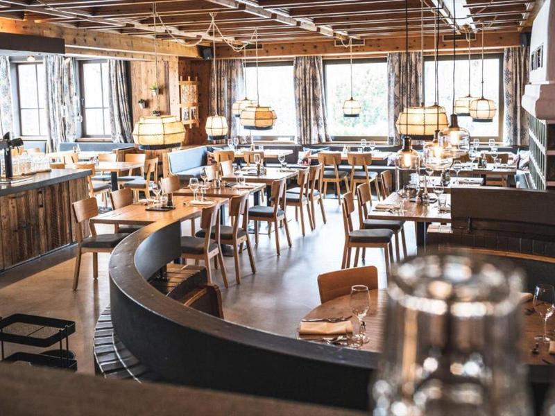 Gemütliches, gut beleuchtetes Restaurant mit Holzmöbeln und großer Fensterfront.