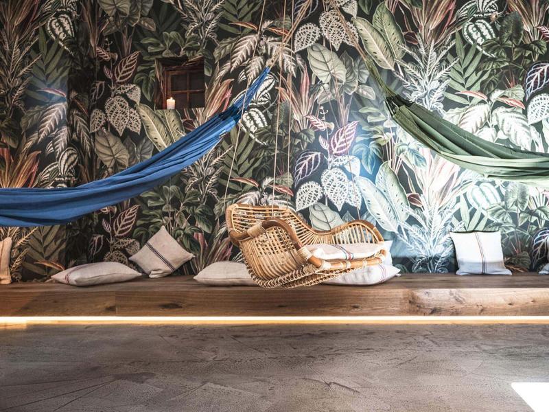 Gemütlicher Innenraum mit Hängematten vor einer bunten Wand mit Pflanzenmuster.