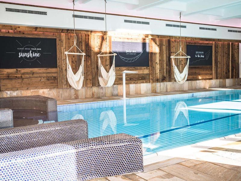 Hallenbad mit Holzpaneelen, Liegestühlen und Makramee-Wanddekorationen.