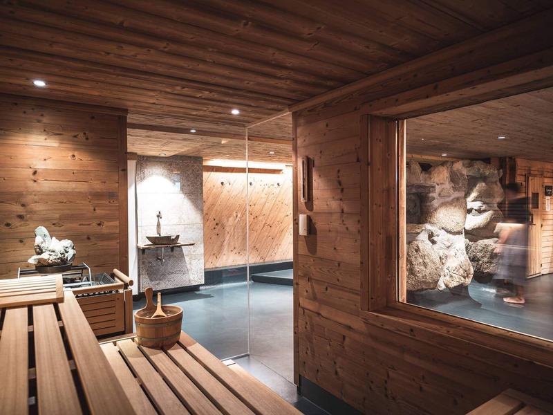 Gemütlicher Spa-Bereich mit Holzwänden, Sauna und Blick auf einen Whirlpool mit Steindekoration.