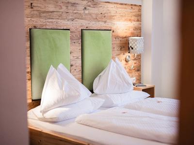 Modern tweepersoonsbed met groen gestoffeerd hoofdeinde en wit beddengoed in hotelkamer.