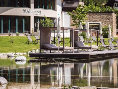 Sonnenliegen am Ufer eines Teichs vor einem Hotelgebäude mit grüner Wiese.