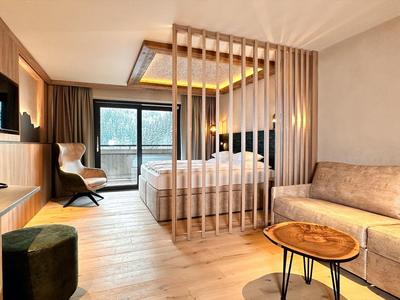 Moderne hotelkamer met houten scheidingswand, bed, comfortabele fauteuil en bank met uitzicht op balkon.