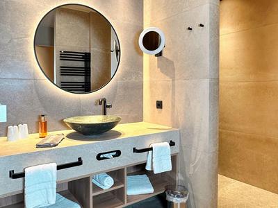 Moderne badkamer met grote ronde spiegel, wastafel en handdoeken onder het aanrecht.